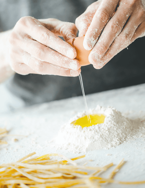Due mani che rompono un uovo per preparare la sfoglia